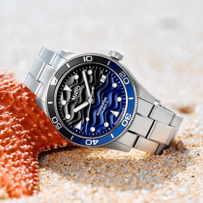 Mido Ocean Star 39mm automatic watch in silver with blue dial and sea-themed details on a sandy beach