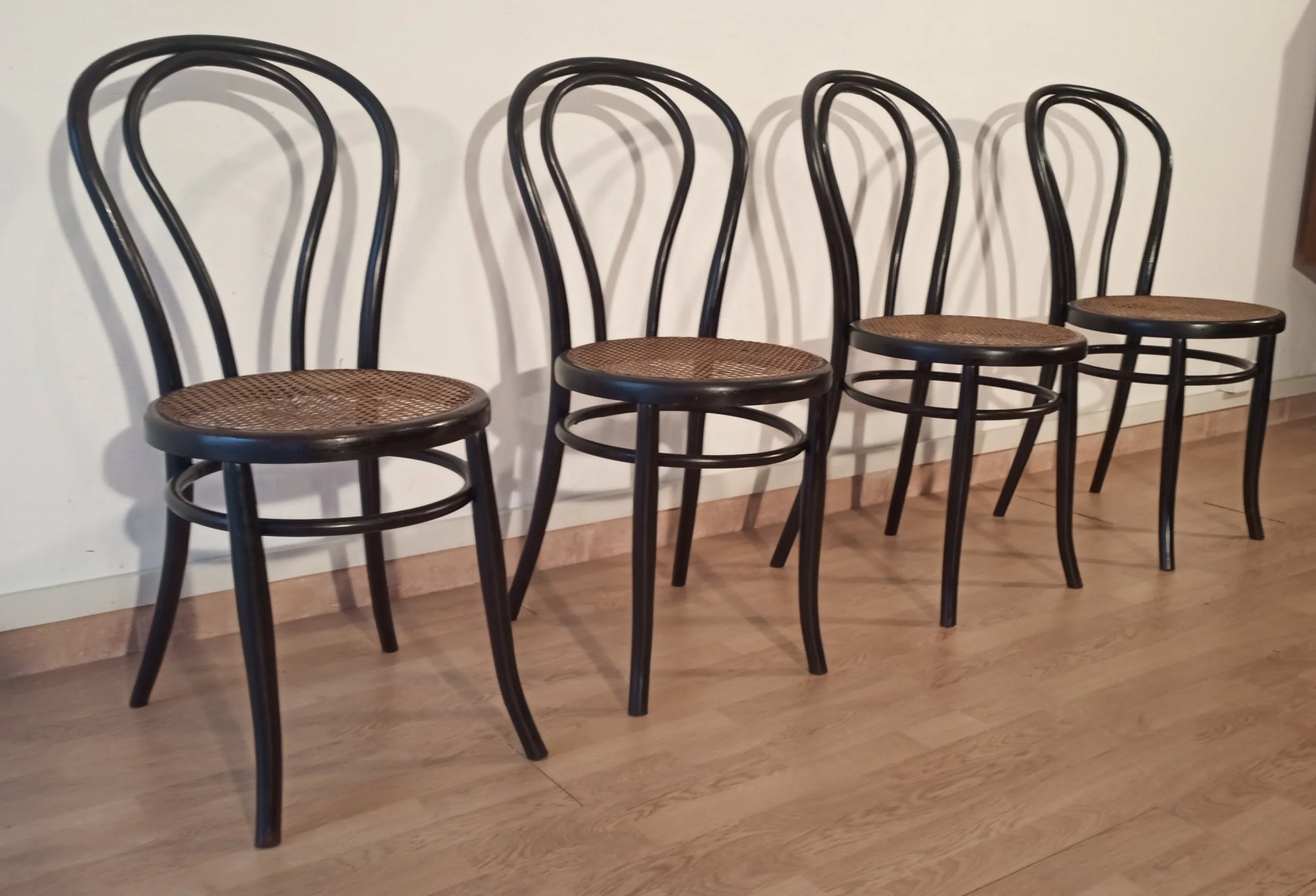 Four bent beech dining chairs in the Thonet Italia style, set with curved backrests and round wooden seats.
